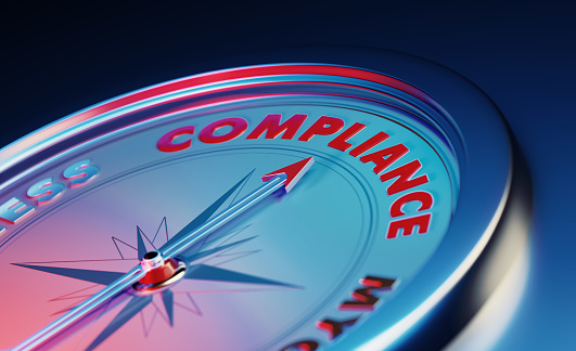 The arrow of the compass is pointing the compliance word over dark blue metallic background. Horizontal composition with copy space. Compliance concept.