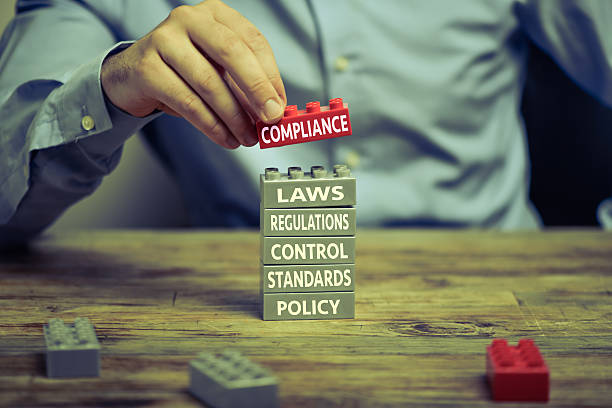 Compliance Man in business shirt playing with toy blocks on wood desk. There are compliance related words printed on the blocks repression stock pictures, royalty-free photos & images