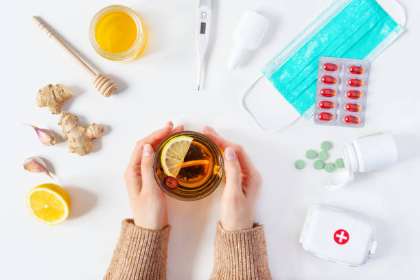 composition of cold and flu treatments. woman hands holding hot tea and different treatments around it. medicaments and herbal medicine concept. - alimentos sistema imunitário imagens e fotografias de stock