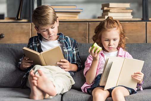 Concentrado Pequeño Hermano Y Hermana Leer Libros En El Sofá En Casa Foto de stock y más banco de imágenes de Alimento - iStock