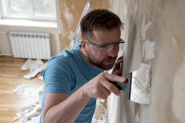 Concentrated man removes old wallpaper from the wall with a spatula in the room. Home repairs. stock photo