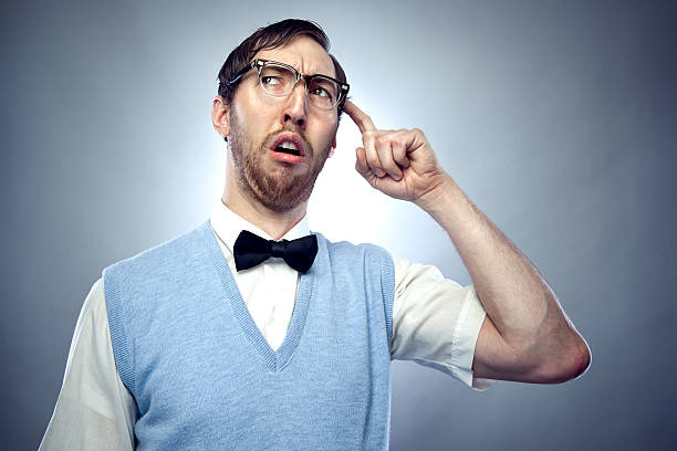 Concentrating Nerd Student Scratching Head Nerdy IT young man wearing a bow tie, blue sweater vest, and horn rimmed glasses makes a confused, goofy face while trying hard to think of something important.  Horizontal on gray / blue background with copy space. worried man funny stock pictures, royalty-free photos & images