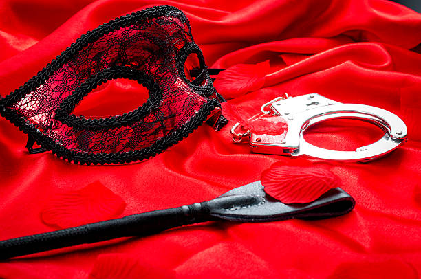 BDSM concept: crop, handcuffs and eyemask on red satin stock photo