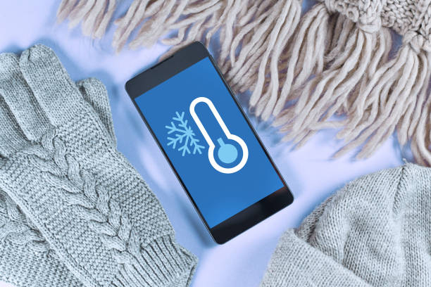 Concept for cold temperatures with snow and minus degrees with mobile phone showing weather forecast surrounded by warm clothes stock photo