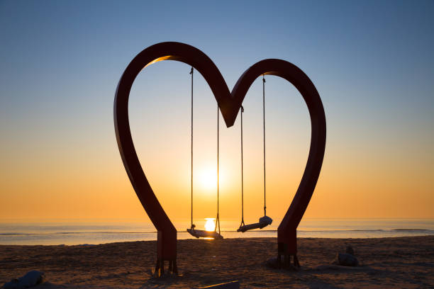 concept love: a heart shape frame with a swing in the background of beautiful orange sea sunrise stock photo