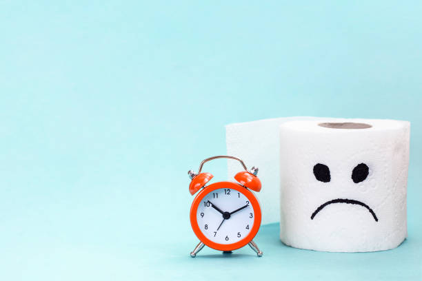 Concept of constipation, indigestion, digestion problem. Alarm clock and toilet paper with sad face Concept of constipation, indigestion, digestion problem. Alarm clock and toilet paper with sad face constipation stock pictures, royalty-free photos & images