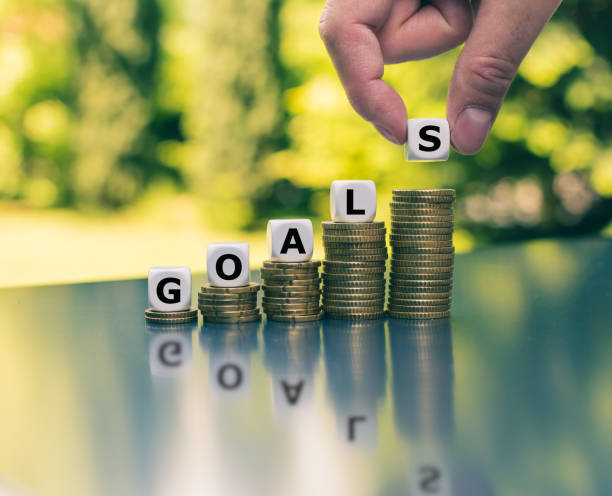 Concept of financial goals. Dice placed on increasing high stacks of coins form the word "GOALS". stock photo