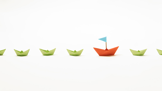 Orange paper boat among of a group of green paper boats on white background. Concept of leadership, individuality, unique.