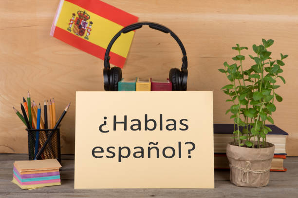 Concept of learning the spanish language - paper with text "¿hablas español?" (hablas espanol), flag of the Spain, books, headphones, pencils on wooden background stock photo