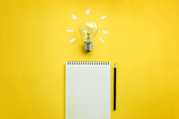 Conceptual brain storming still life. Flat lay of light bulb and empty memo pad and pencil on yellow background with texts. writing activity stock pictures, royalty-free photos & images