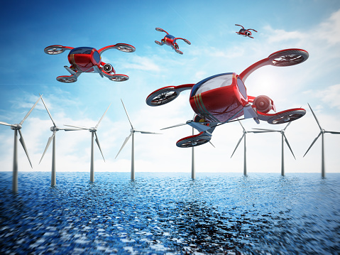 Conceptual eVTOL (electric vertical take-off and landing) aircrafts flying over the sea and wind turbines.