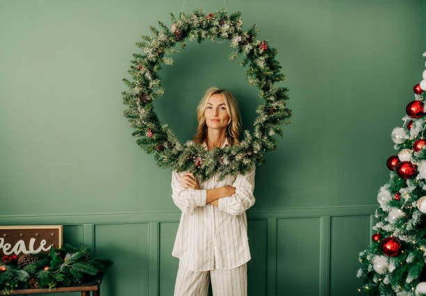 Conceptual portrait of young elegant woman framed by christmas wreath against wall in living room stock photo