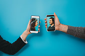 Conceptual shot of a young couple connecting together with a smartphone during social distancing. They are holding smart phones against a blue background.