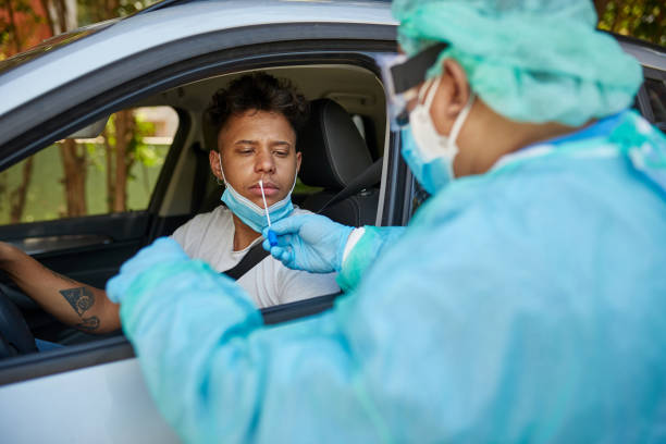 Concerned Man Getting COVID-19 Nasal Swab Test at Drive-Thru Healthcare professional in protective workwear preparing to do nasal swab testing on Afro-Caribbean man in early 20s at drive-thru site. infectious disease photos stock pictures, royalty-free photos & images