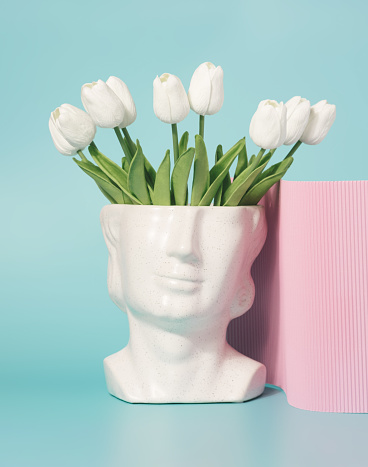 Concrete head sculpture with tulip flowers on a pastel blue background. Spring, summer artistic concept.