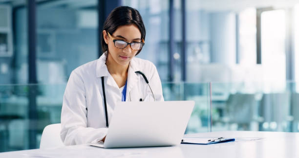 Conducting further research to improve her healthcare services Shot of a young doctor using a laptop in a hospital general practitioner photos stock pictures, royalty-free photos & images