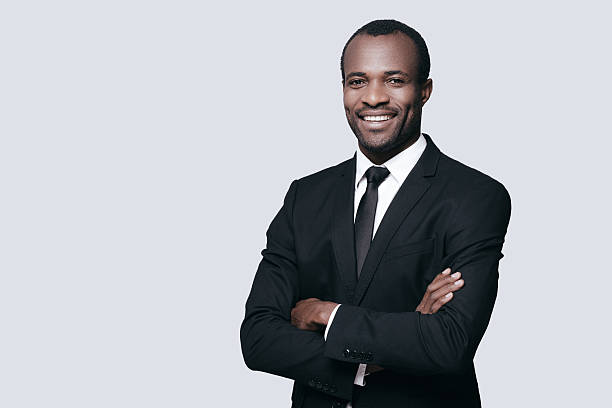 Confidence and style. Handsome young African man in formalwear keeping arms crossed and looking at camera while standing against grey background business suit stock pictures, royalty-free photos & images