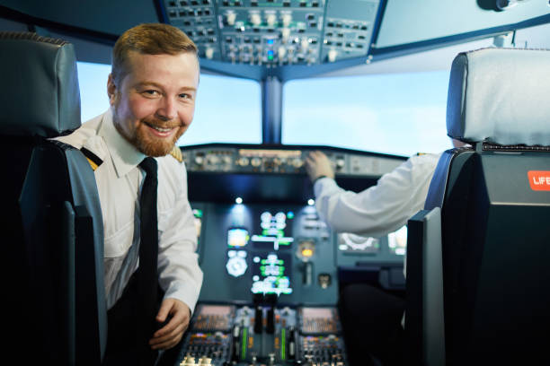 Confident bearded pilot in cockpit Cheerful confident bearded pilot in white shirt and black tie sitting in armchair and turning back to look at camera in cockpit pilot stock pictures, royalty-free photos & images