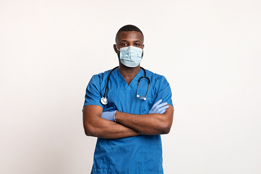 Confident black doctor in face mask and gloves over white studio background, copy space