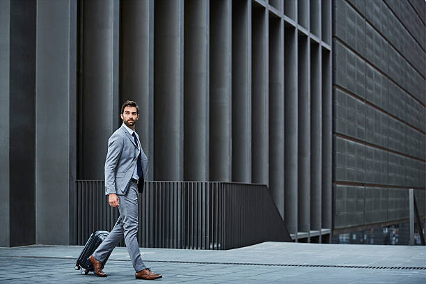 Confident businessman with bag against building Full length of confident businessman with luggage. Side view of executive is walking against building. Professional is looking away. business suit stock pictures, royalty-free photos & images