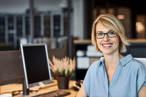 Portrait of confident businesswoman smiling in office. Female professional is with short blond hair. She is in textile factory.