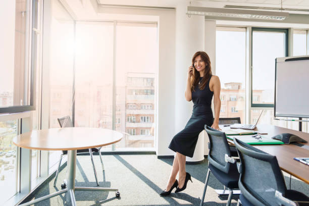 Confident businesswoman talking with somebody on mobile phone while standing at the office stock photo