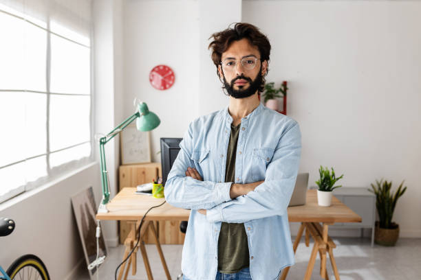 Confident creative businessman with crossed arms standing in workplace stock photo