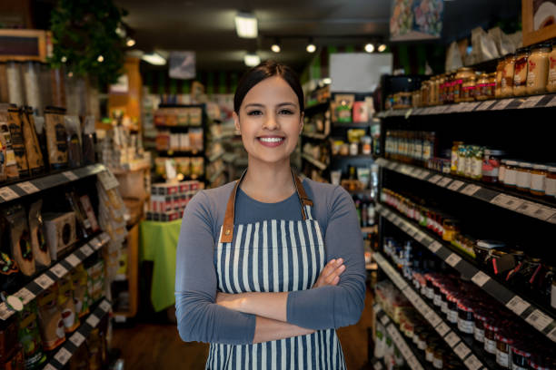 confident female business owner of a supermarket standing between shelves while facing camera smiling - trabalhadora de colarinho branco imagens e fotografias de stock
