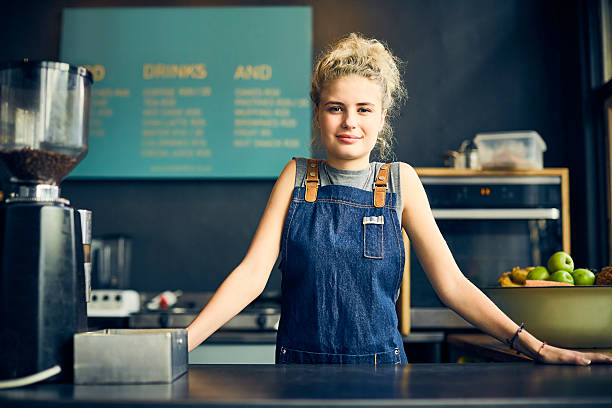 Confident female cafe owner leaning on cafe counter stock photo