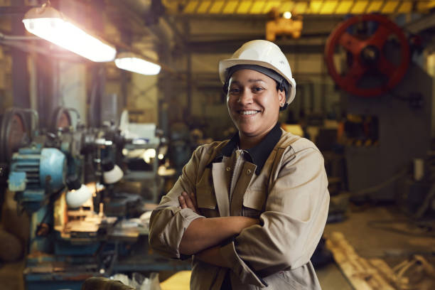 Confident Female Factory Worker Waist up portrait of mixed-race female worker posing confidently while standing with arms crossed in factory workshop blue collar worker stock pictures, royalty-free photos & images
