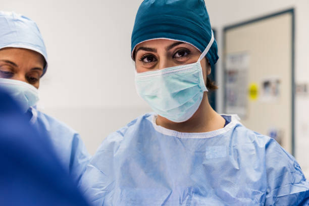 Confident focused female surgeon Confident mid adult female surgeon looks at the camera while performing a successful surgical procedure. medical scrubs photos stock pictures, royalty-free photos & images