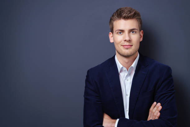 Confident handsome young businessman Confident handsome young businessman in a stylish jacket standing with folded arms smiling at the camera over a dark background with copy space germany photos stock pictures, royalty-free photos & images