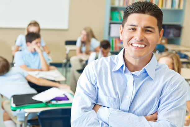 Confident Hispanic private school teacher in classroom Handsome mid adult Hispanic high school teacher smiles while standing in front of his classroom with his arms crossed. middle school teacher stock pictures, royalty-free photos & images