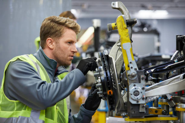 Confident male engineer examining car chassis Confident mid adult engineer examining car chassis at automobile industry. Handsome male supervisor is working on car part in factory. He is wearing reflective clothing. car plant stock pictures, royalty-free photos & images