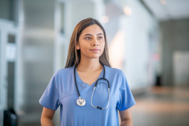 Confident medical student wearing medical scrubs A young female medical student is standing inside a medical building. She is wearing blue medical scrubs and is looking away from the camera. female nurse stock pictures, royalty-free photos & images