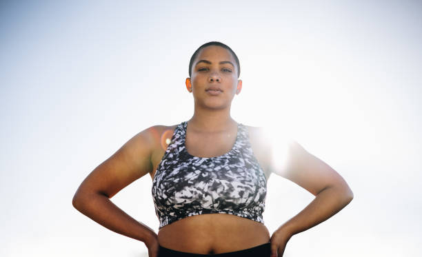 Confident plus size female model in sportswear Plus size female in sportswear standing with her hands on hips. Confident female standing outdoors with sun shining from behind. body positive stock pictures, royalty-free photos & images