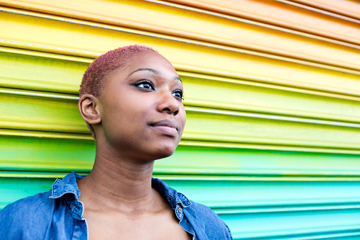 Beautiful teen looks off in the distance as she stands infront of rainbow-colored wall (selective focus)