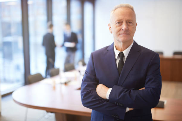 Confident Senior Businessman Posing in Conference Room Waist up portrait of successful senior businessman standing with arms crossed in conference room and looking at camera, copy space ceo stock pictures, royalty-free photos & images