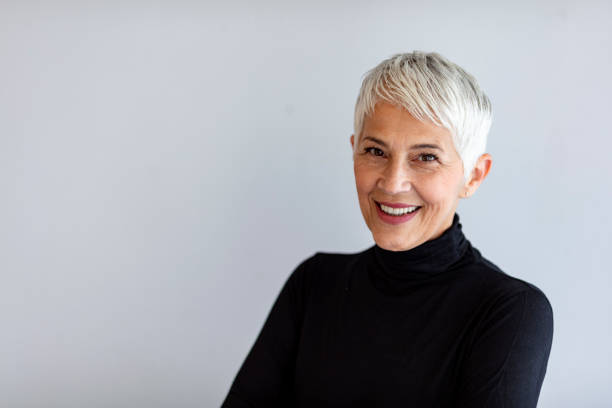 Confident senior woman Close up portrait of beautiful older gray hair woman smiling and standing by gray wall wearing black turtleneck. mature women beauty beautiful fashion model stock pictures, royalty-free photos & images