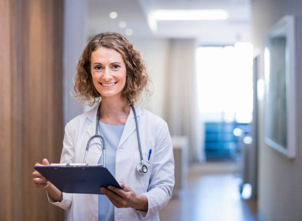 Confident smiling female doctor with clipboard Smiling female doctor with clipboard in corridor. Portrait of confident medical professional is wearing lab coat and stethoscope. She is standing at hospital. female doctor stock pictures, royalty-free photos & images