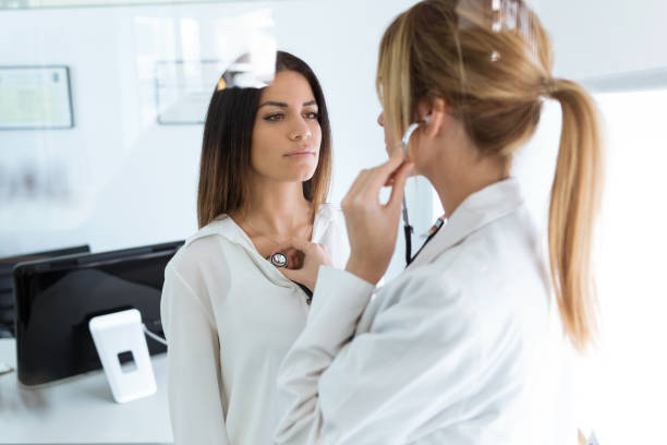 Confident woman being examined with stethoscope by doctor in the medical consultation. Shot of confident woman being examined with stethoscope by doctor in the medical consultation. general view stock pictures, royalty-free photos & images
