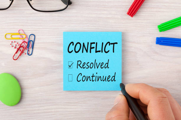 Conflict writing on note concept Hand writing Conflict, Resolved and Continued on note with marker pen and glasses on wooden desk. Business Concept. Top view. conflict stock pictures, royalty-free photos & images