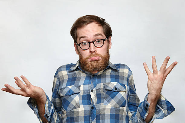 Confused bearded man in eyeglasses shrugging his shoulders Man with beard and eyeglasses shrugging his shoulders in confusion, arms raised, isolated on gray confusion stock pictures, royalty-free photos & images
