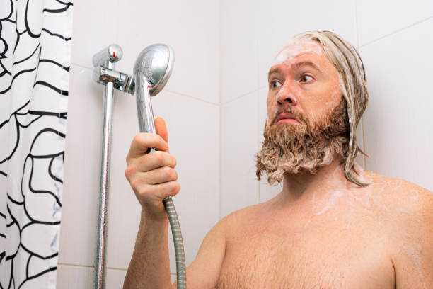 Confused bearded man with soapy head standing in the bathroom and looking at the shower while the water supply has stopped. No water coming from tap. Confused bearded man with soapy head standing in the bathroom and looking at the shower while the water supply has stopped. No water coming from tap worried man funny stock pictures, royalty-free photos & images