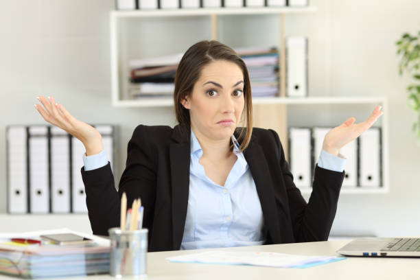 Confused businesswoman looking at camera Front view portrait of a confused businesswoman shrugging shoulders looking at camera at office confusion photos stock pictures, royalty-free photos & images