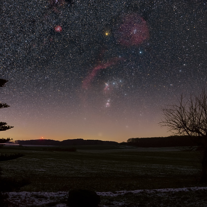Constellation of Orion with its nebulae on the starry night sky over rural landscape