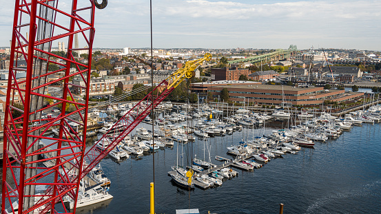 Harbor with many yachts and boats in Boston, Massachusetts, and construction crane at the front.