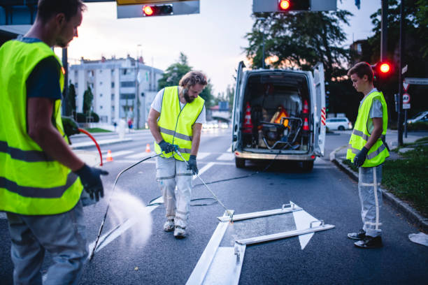 Construction Crew Member Spray Painting Turn Arrow at Dusk Three-man construction crew in reflective vests spray painting turn arrow marking in Central European capital city. dividing line road marking stock pictures, royalty-free photos & images
