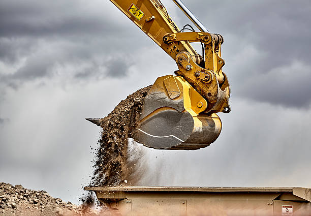 Construction industry excavator bucket loading gravel closeup Construction industry heavy equipment excavator moving gravel at jobsite quarry with stormy skies earth mover stock pictures, royalty-free photos & images