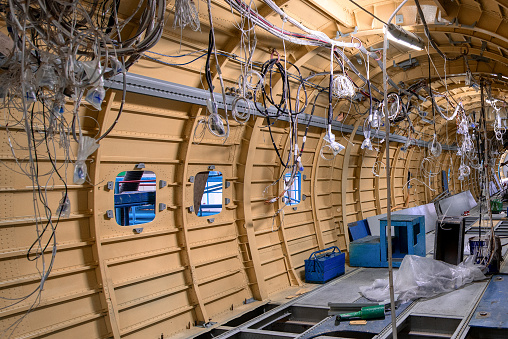 Construction of a new aircraft. Many electrical cables and wires hang from the sides of the fuselage.